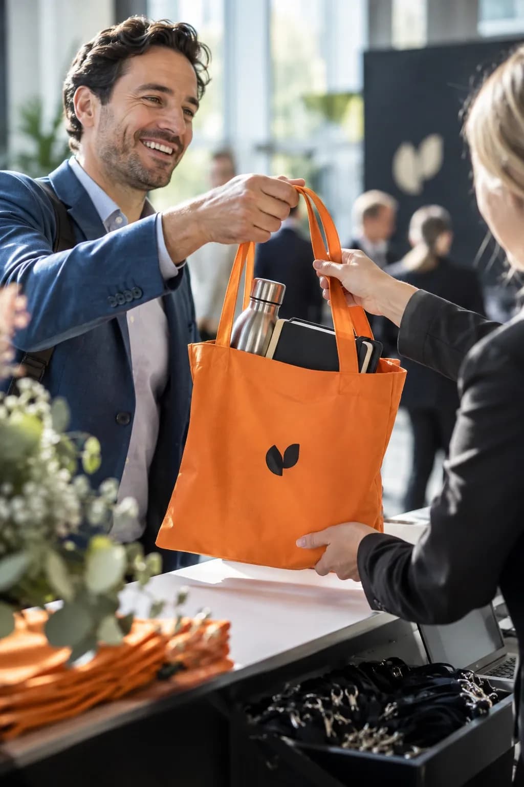 Man tar emot en orange tygkasse med logotyp, termosflaska och block vid en registreringsdisk